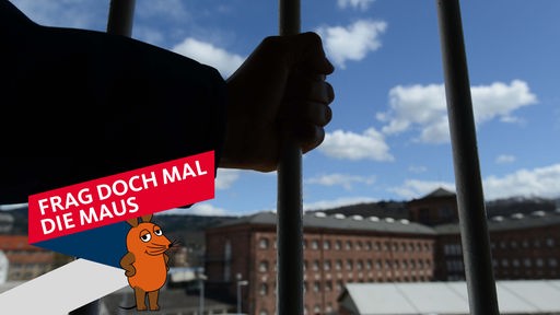 Eine Hand umfasst in der Justizvollzugsanstalt in Freiburg einen Gitterstab vor einem vergitterten Fenster.